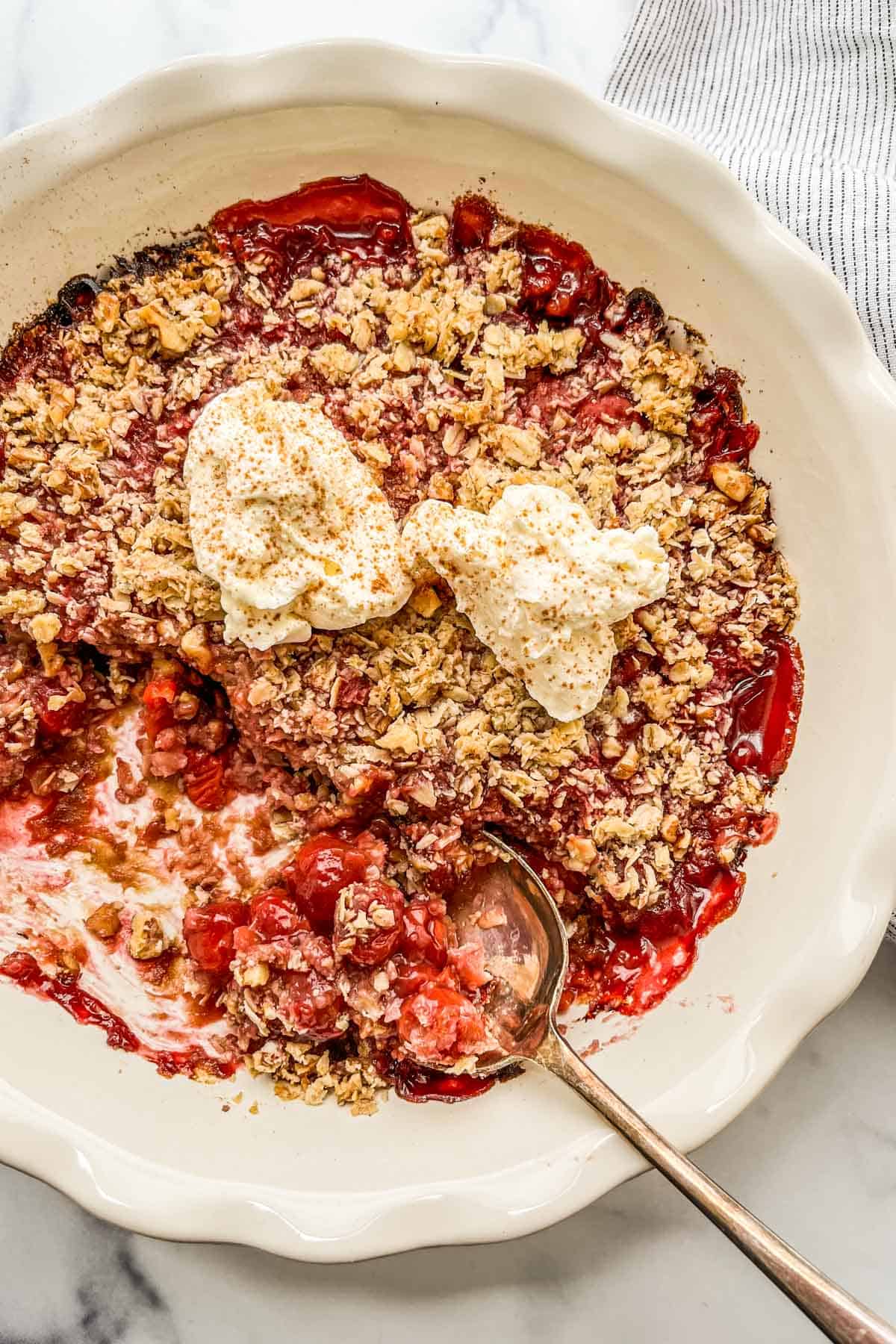 Sour cherry crisp being spooned out of a pie plate.