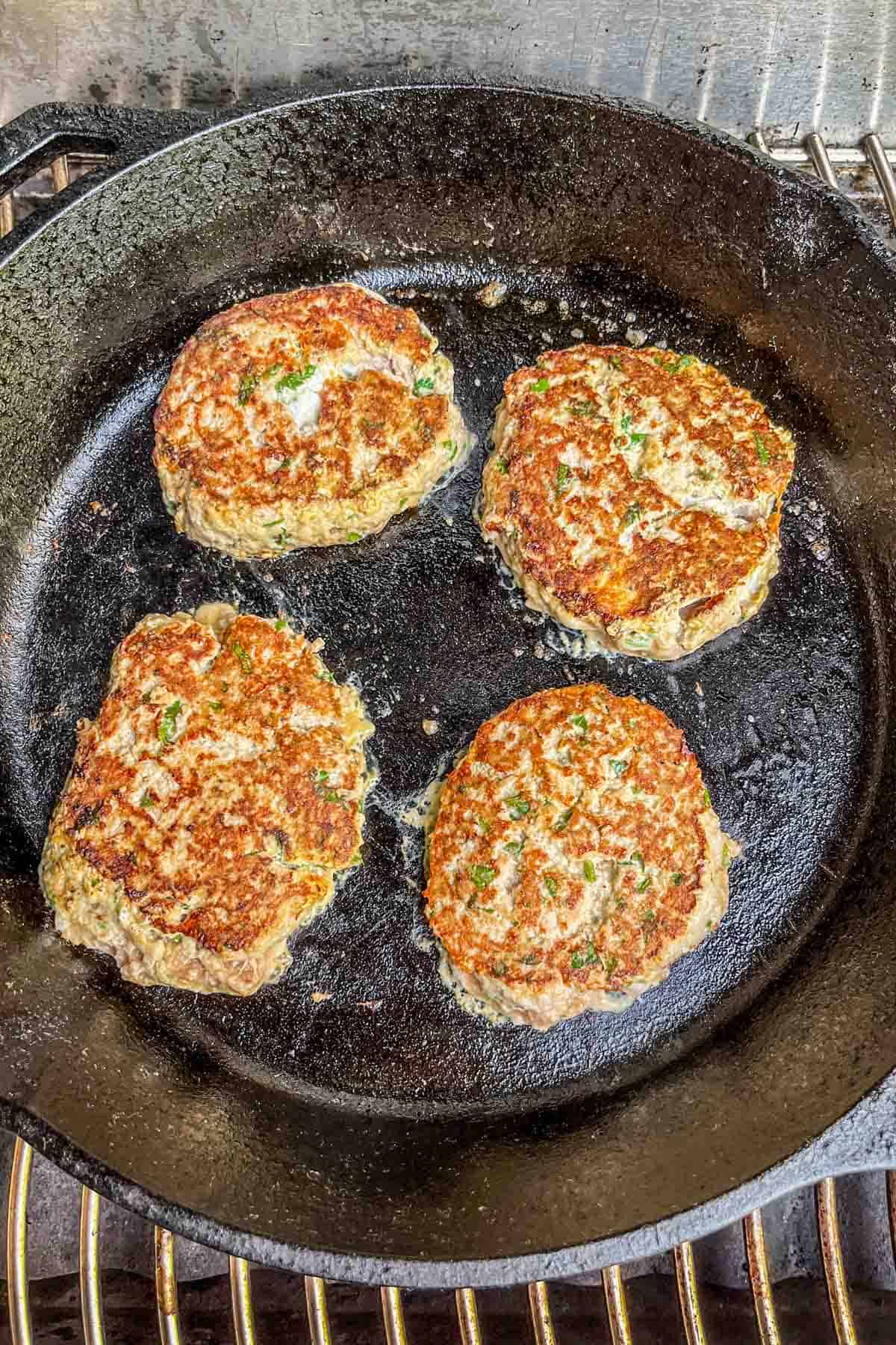 Four turkey burgers in a cast iron pan on a grill.