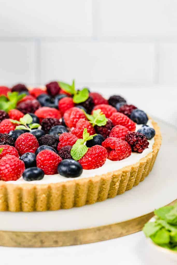 A berry yogurt tart with almond crust on a cake plate.