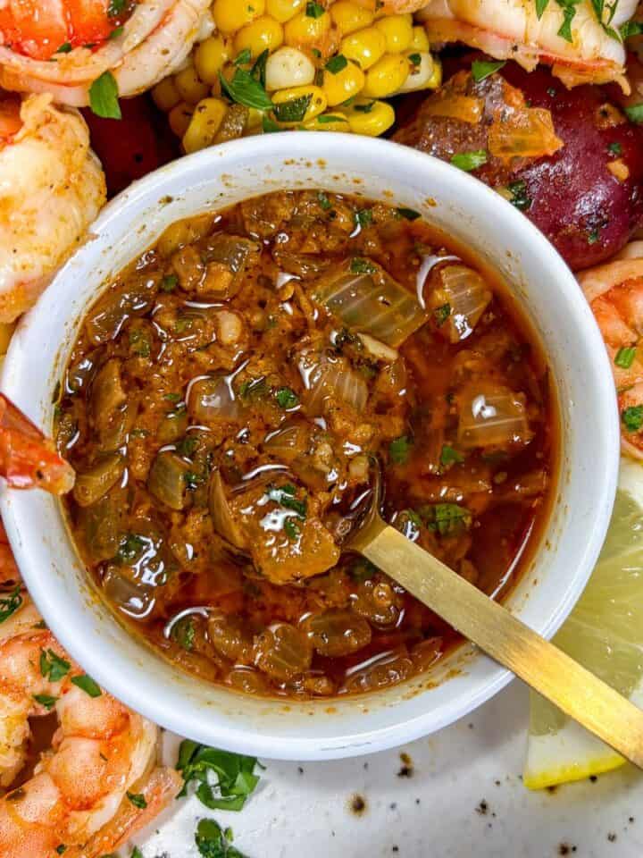Cajun butter sauce for seafood in a white bowl, surrounded by shrimp, potatoes, and corn.
