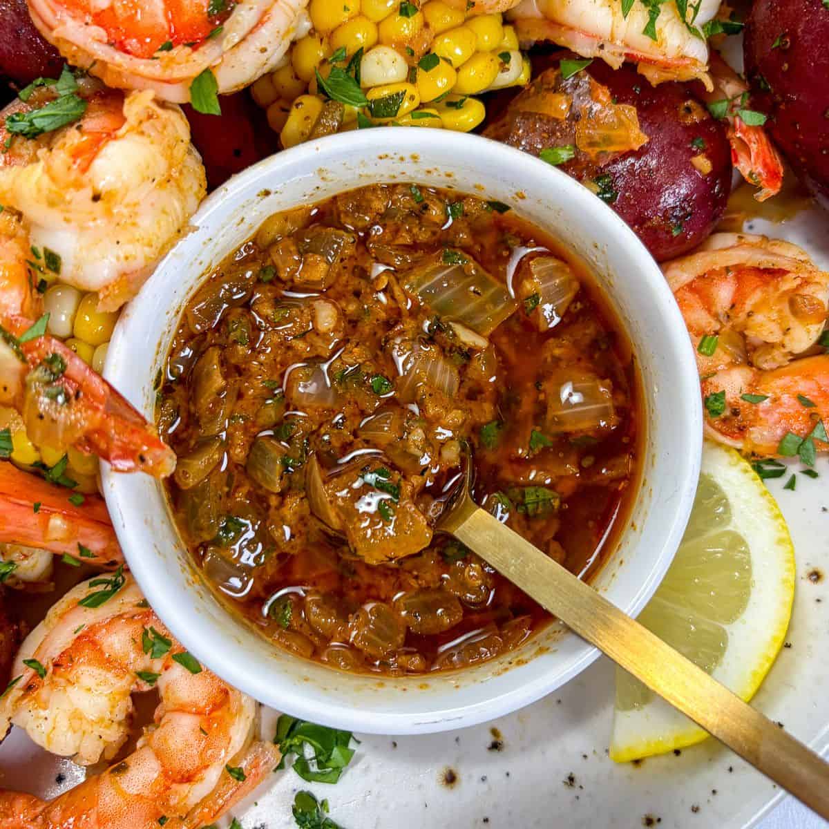 Cajun butter sauce for seafood in a white bowl, surrounded by shrimp, potatoes, and corn.