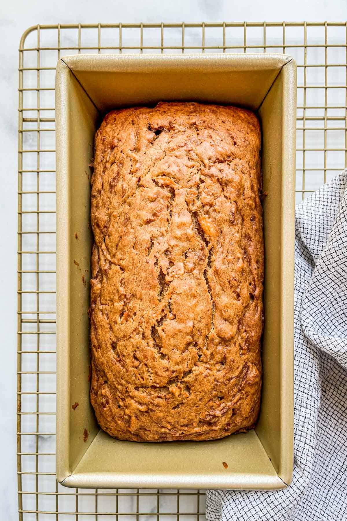 A loaf of cantaloupe bread in a bread pan on a cooling rack.