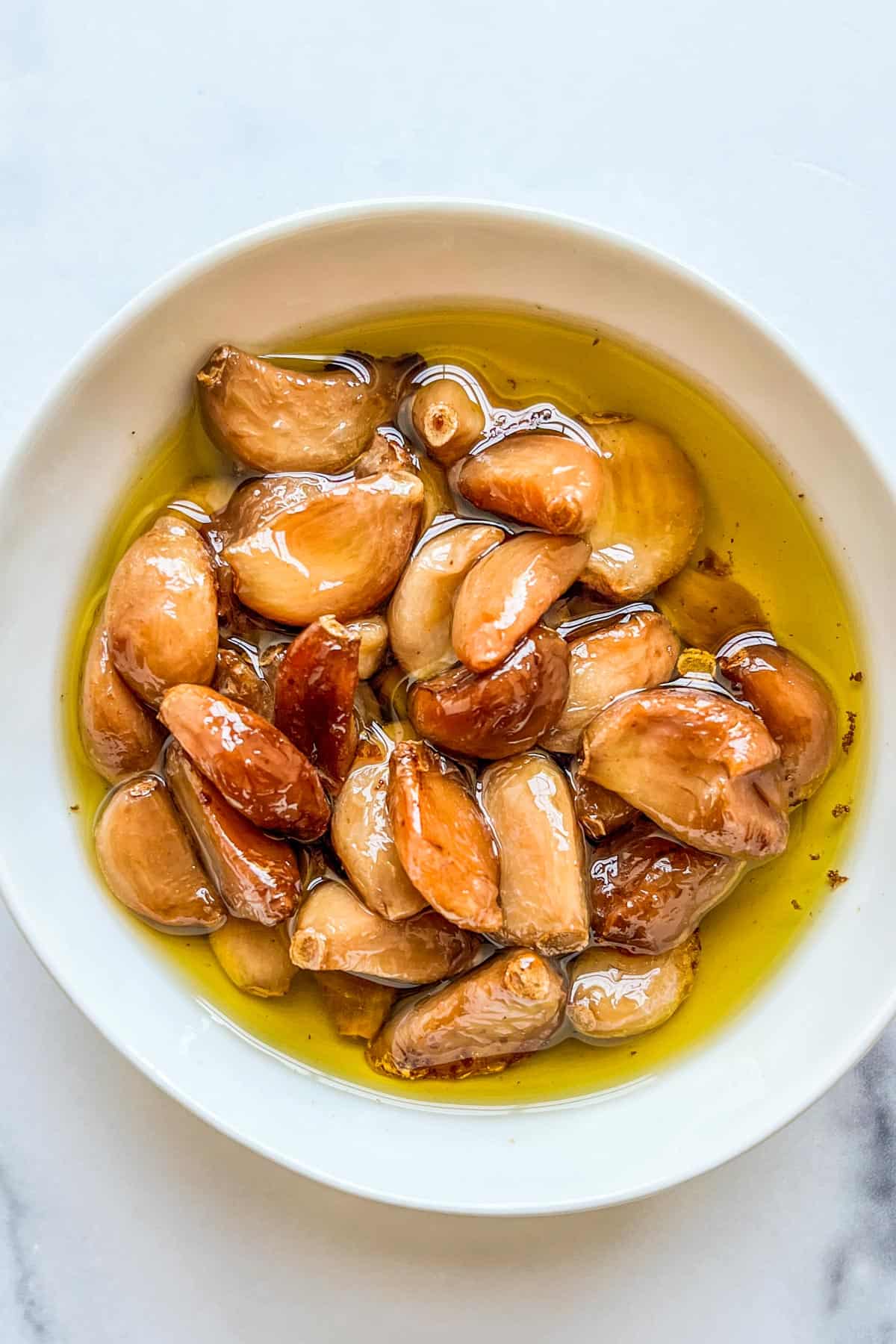 Garlic confit in oil in a white bowl.