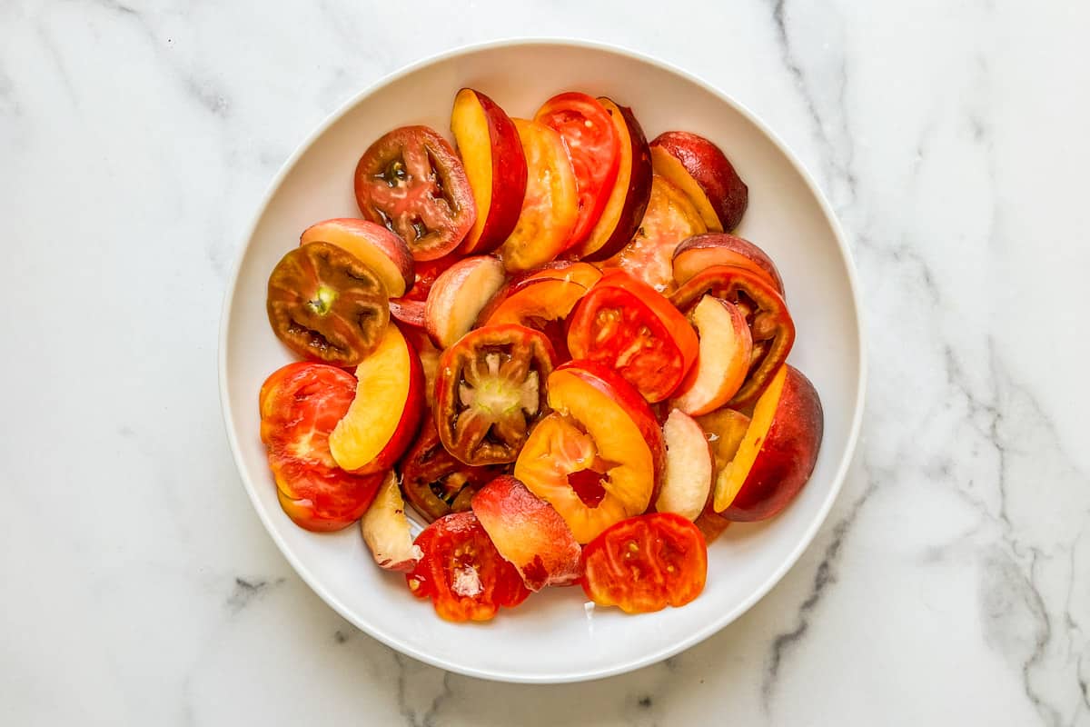 Sliced heirloom tomatoes and stone fruit in a bowl.
