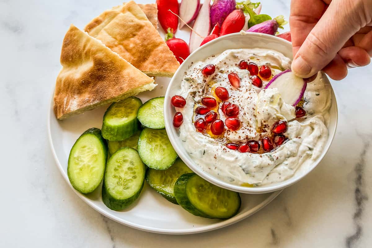 A radish being dipped into tahini yogurt sauce.