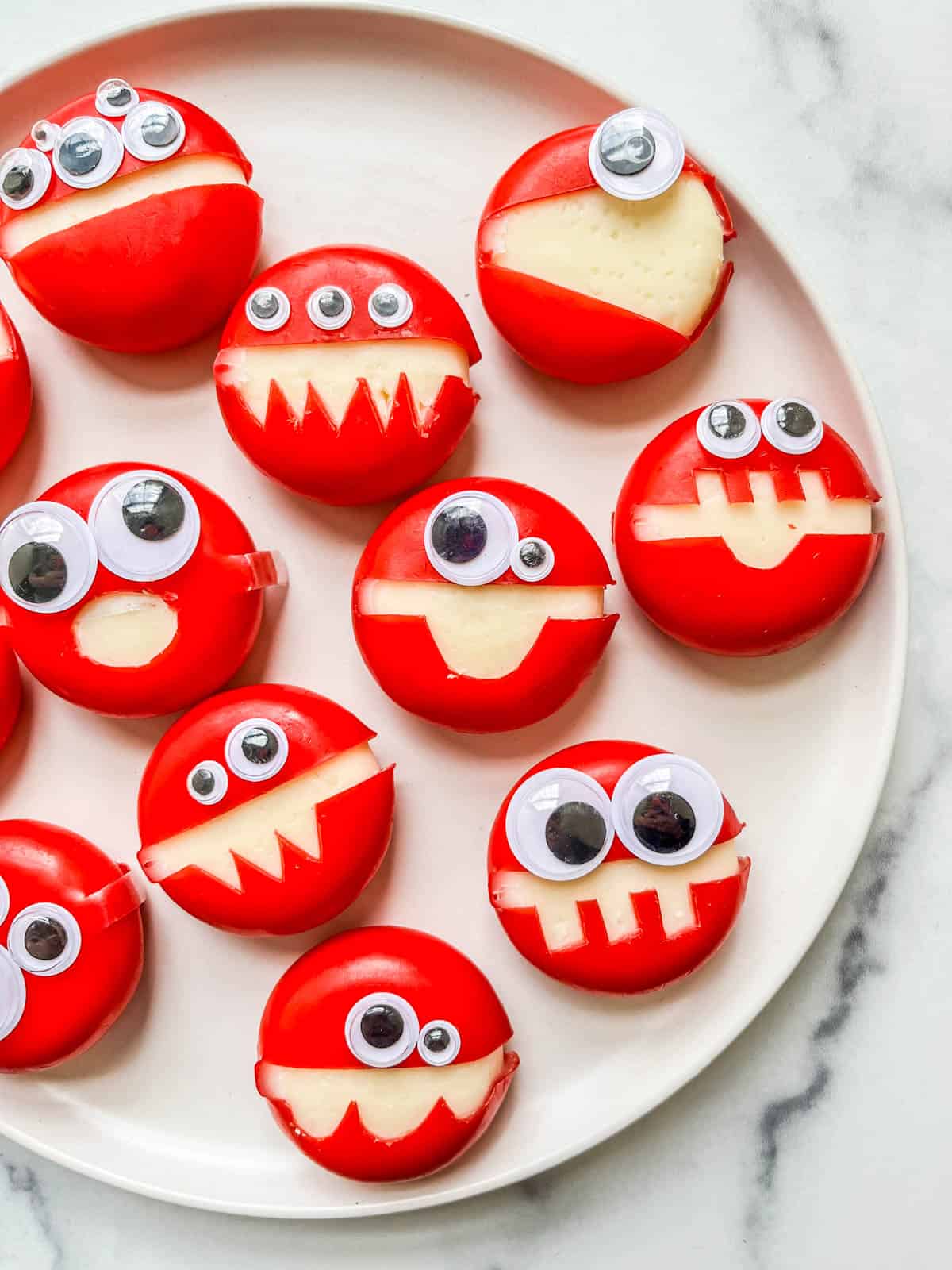 Halloween cheese monsters on a white plate.