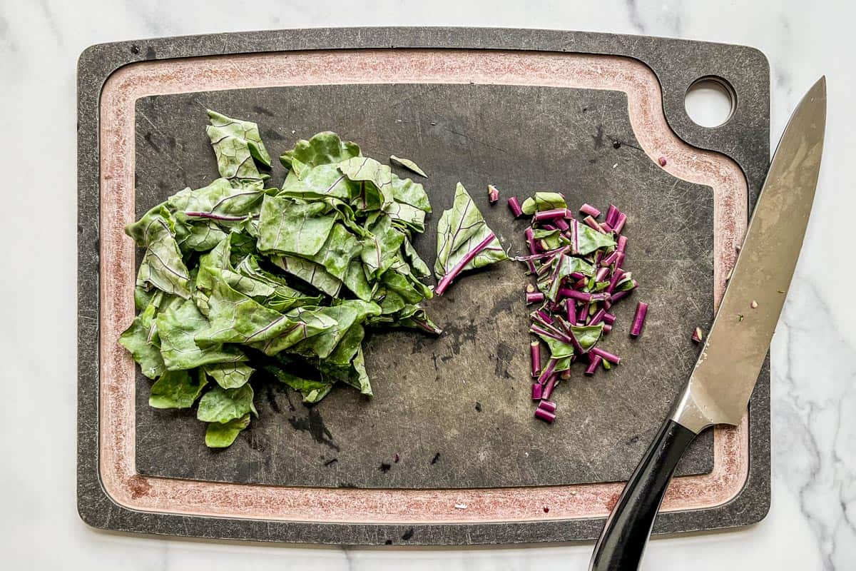 Diced kohlrabi stems and roughly chopped kohlrabi greens on a cutting board.