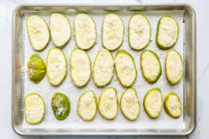 Slices of squash topped with parmesan on a baking sheet.