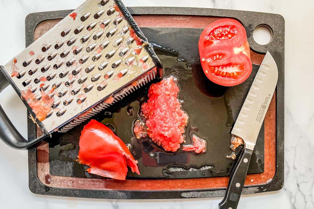 Grated tomatoes and a box grater on a cutting board.