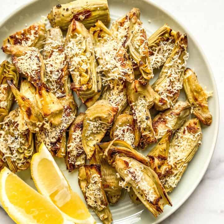 Roasted artichoke hearts with parmesan on a green plate.