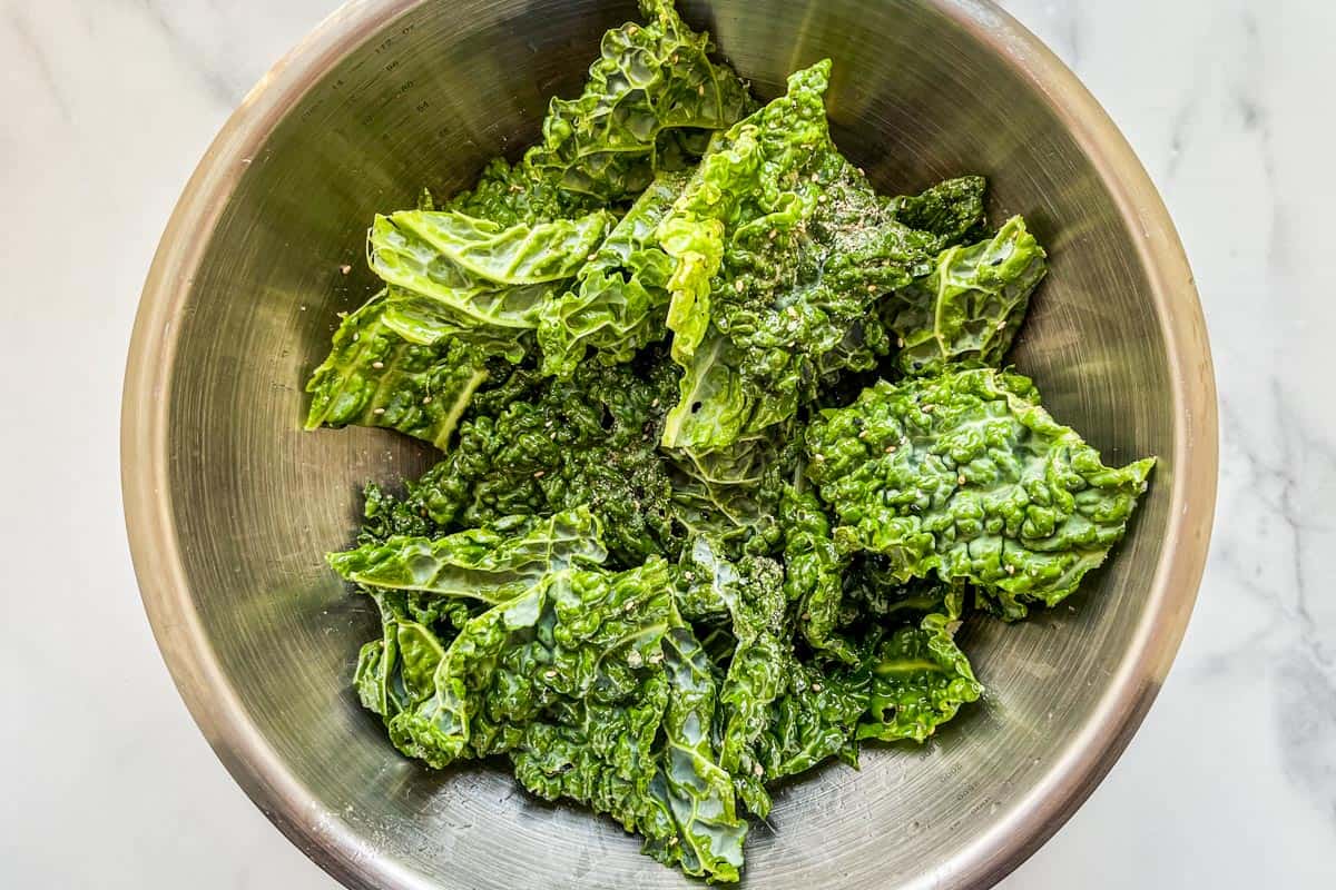 Pieces of savoy cabbage, tossed with olive oil and spices in a mixing bowl.
