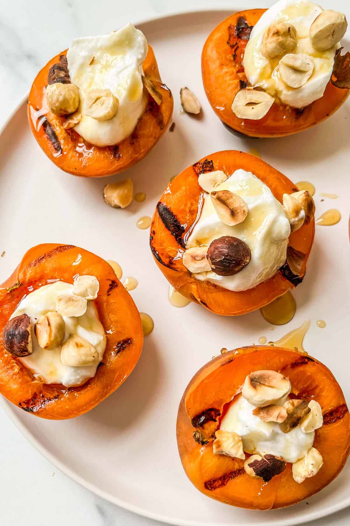 Grilled apricots with yogurt, honey, and hazelnuts on a plate.