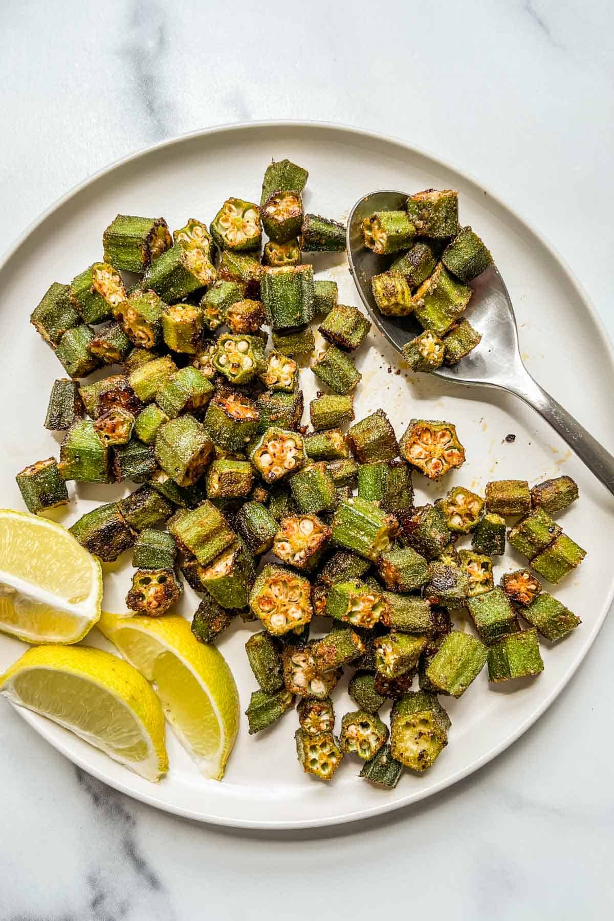 Oven roasted okra on a white plate with a spoon.