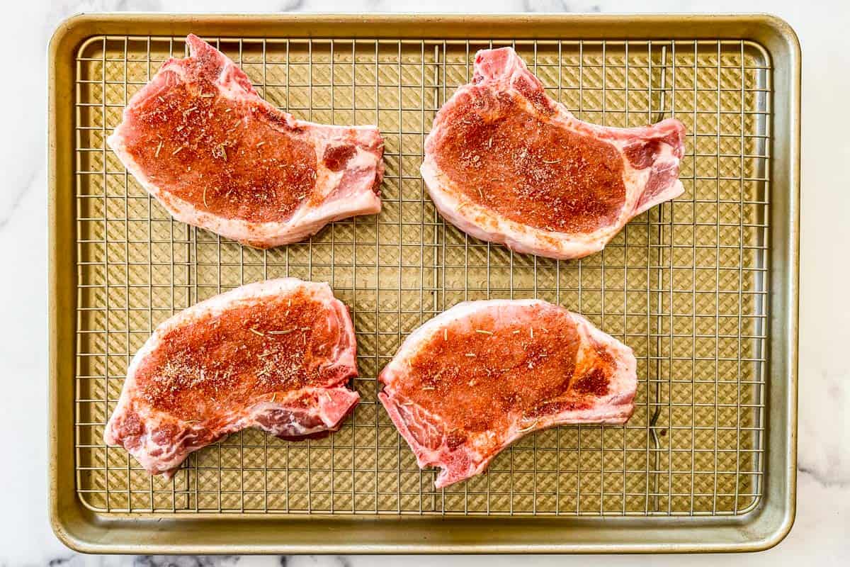 Four pork chops dry brining on a rack and rimmed baking sheet.