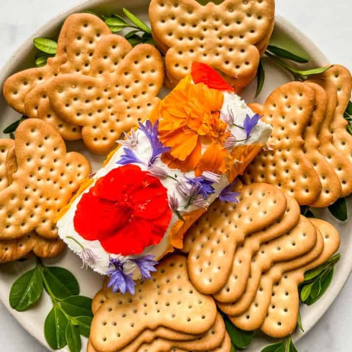 An edible flower cheese log surrounded by crackers.