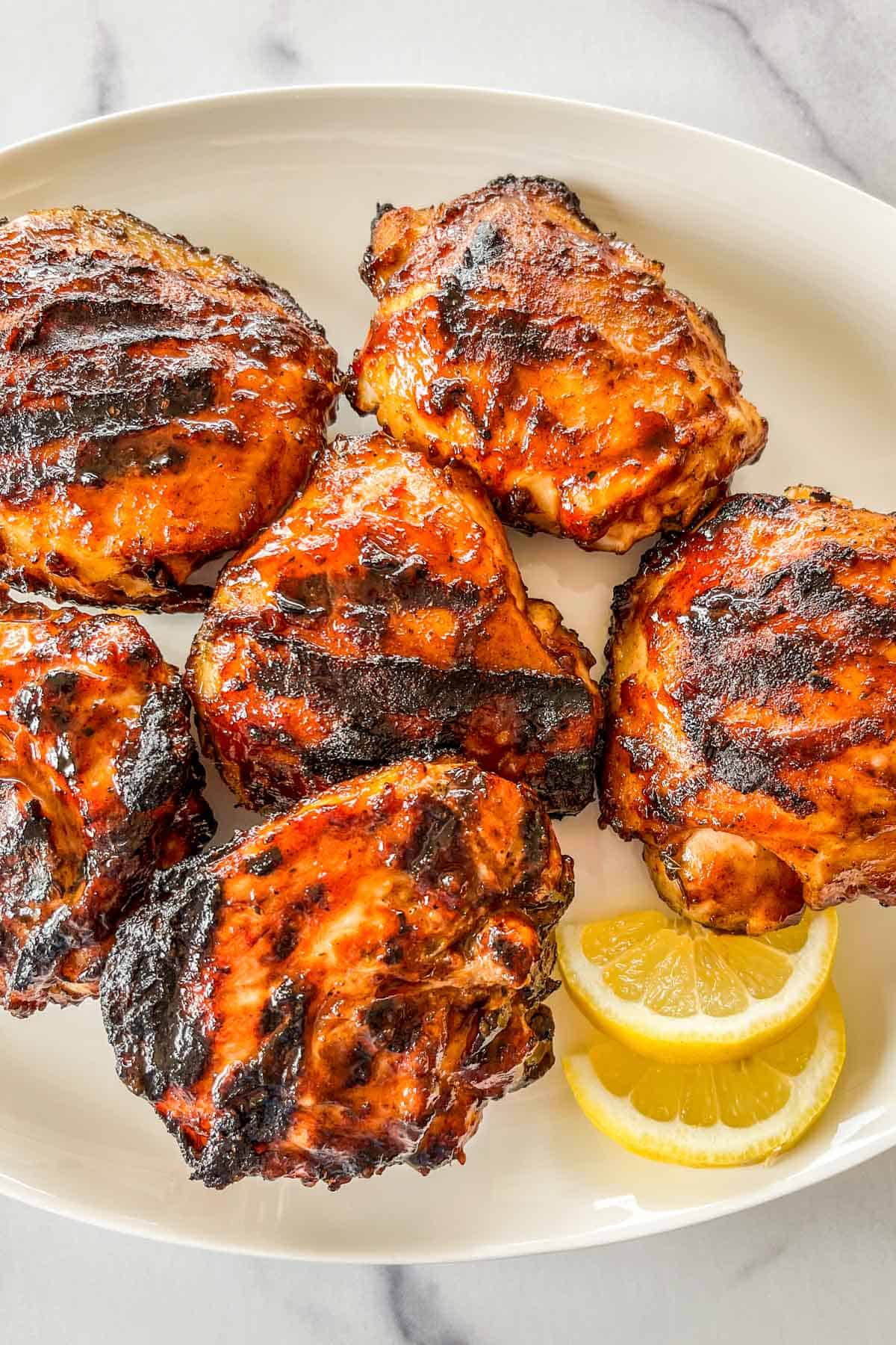 Grilled chicken thighs topped with barbecue sauce on a platter.