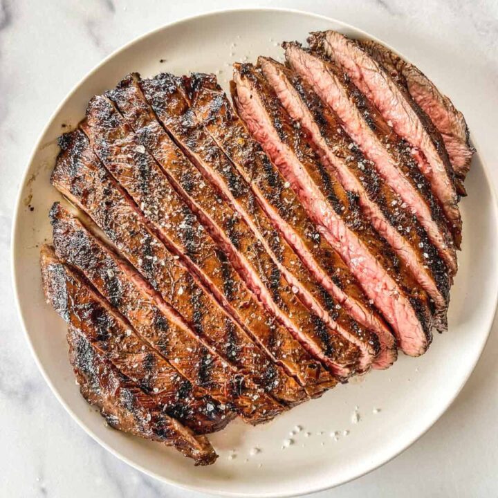 Grilled sliced flank steak on a white plate.