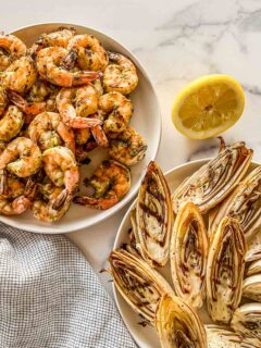 A large bowl of pesto grilled shrimp next to a plate of grilled endives.