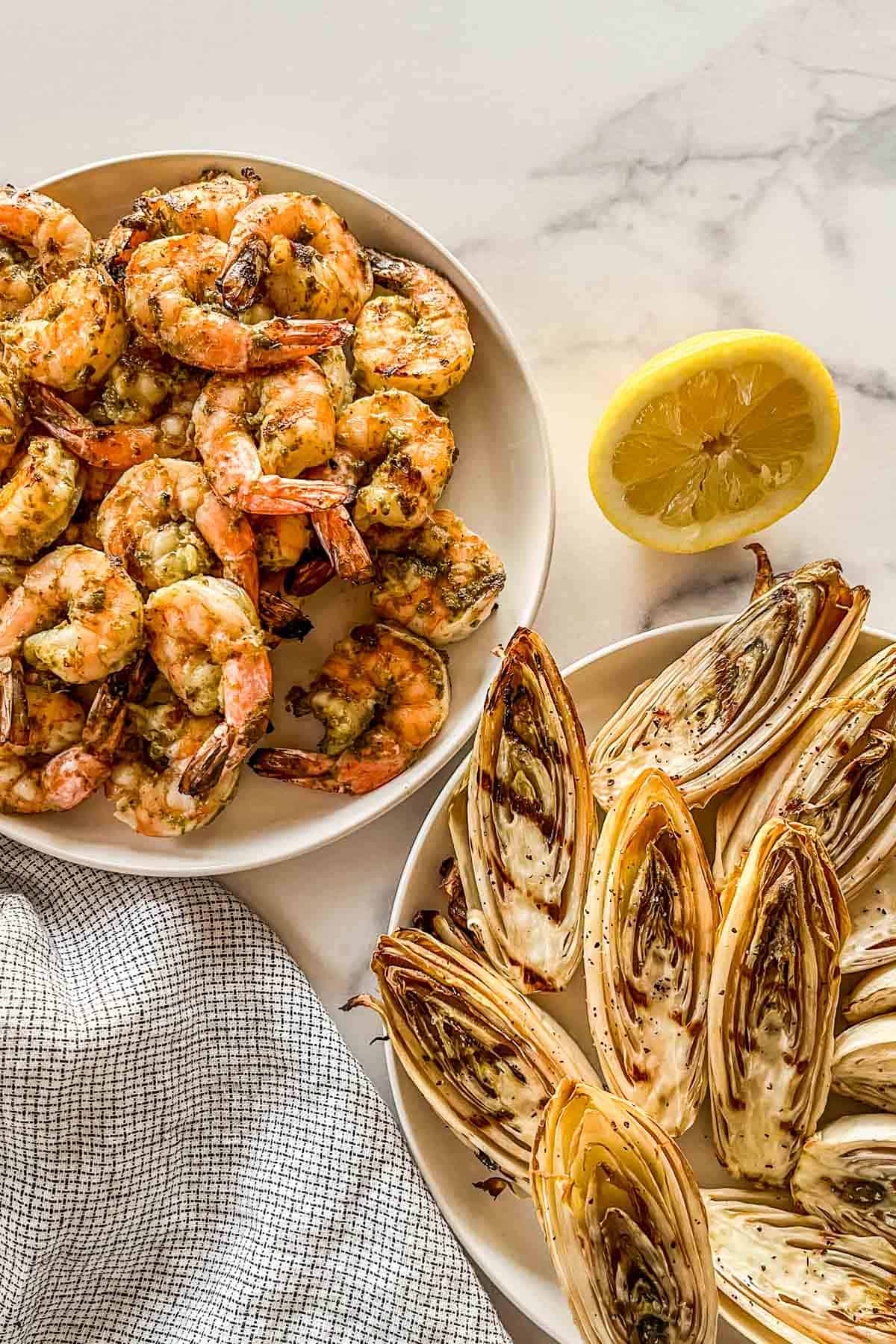 A large bowl of pesto grilled shrimp next to a plate of grilled endives.