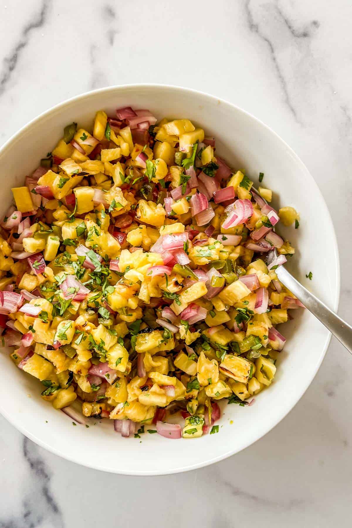 Pineapple salsa in a white bowl with a silver serving spoon.