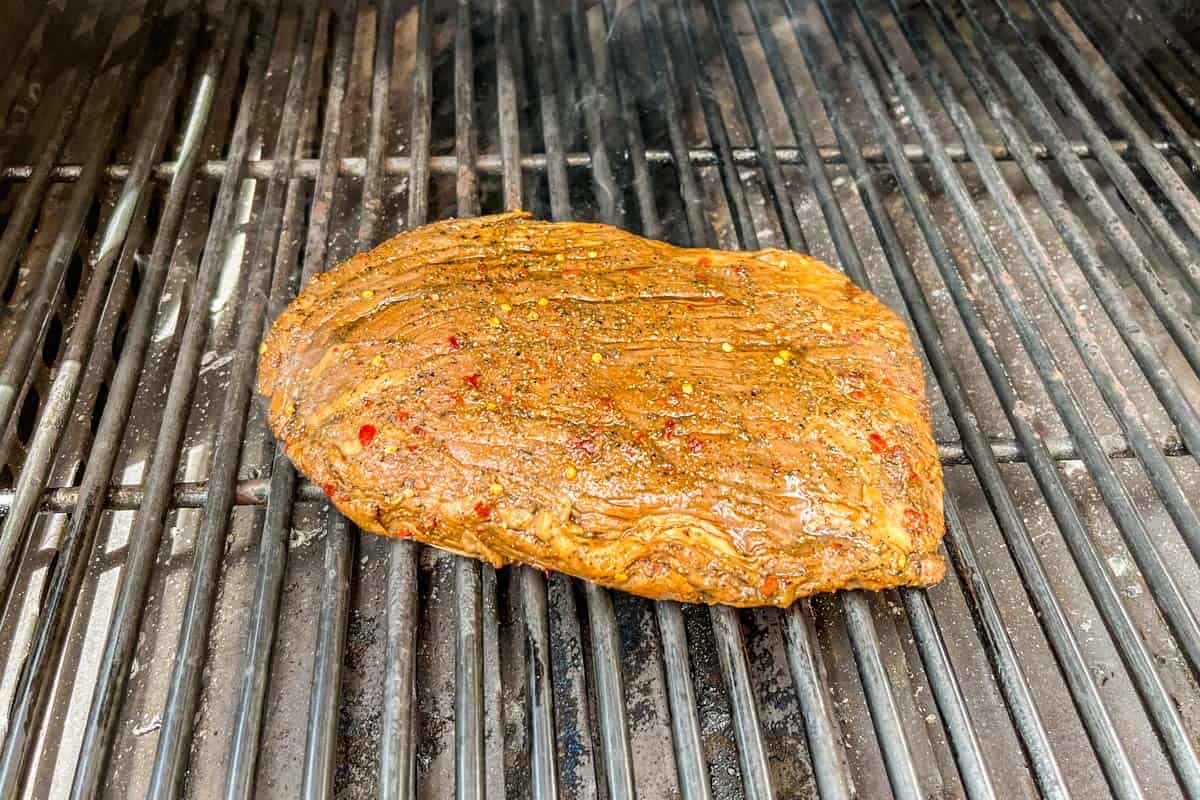 A flank steak with marinade on a grill.