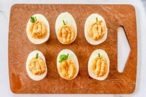 Six pumpkin deviled eggs on a cutting board.