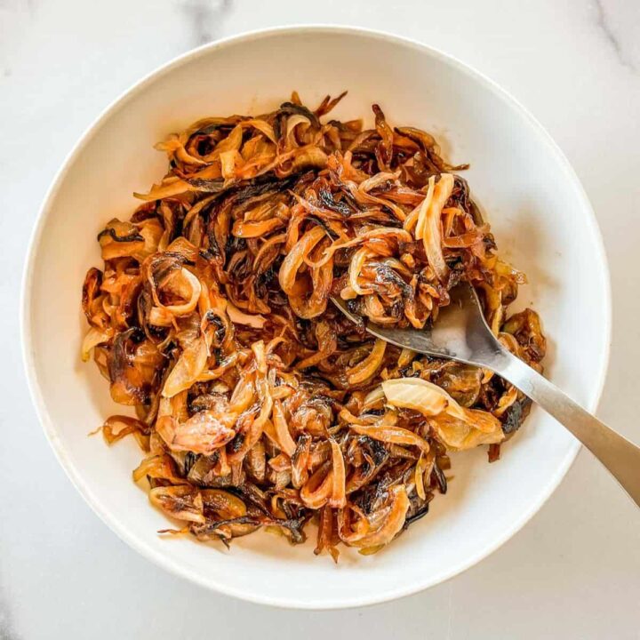 Caramelized onions in a white bowl with a spoon.