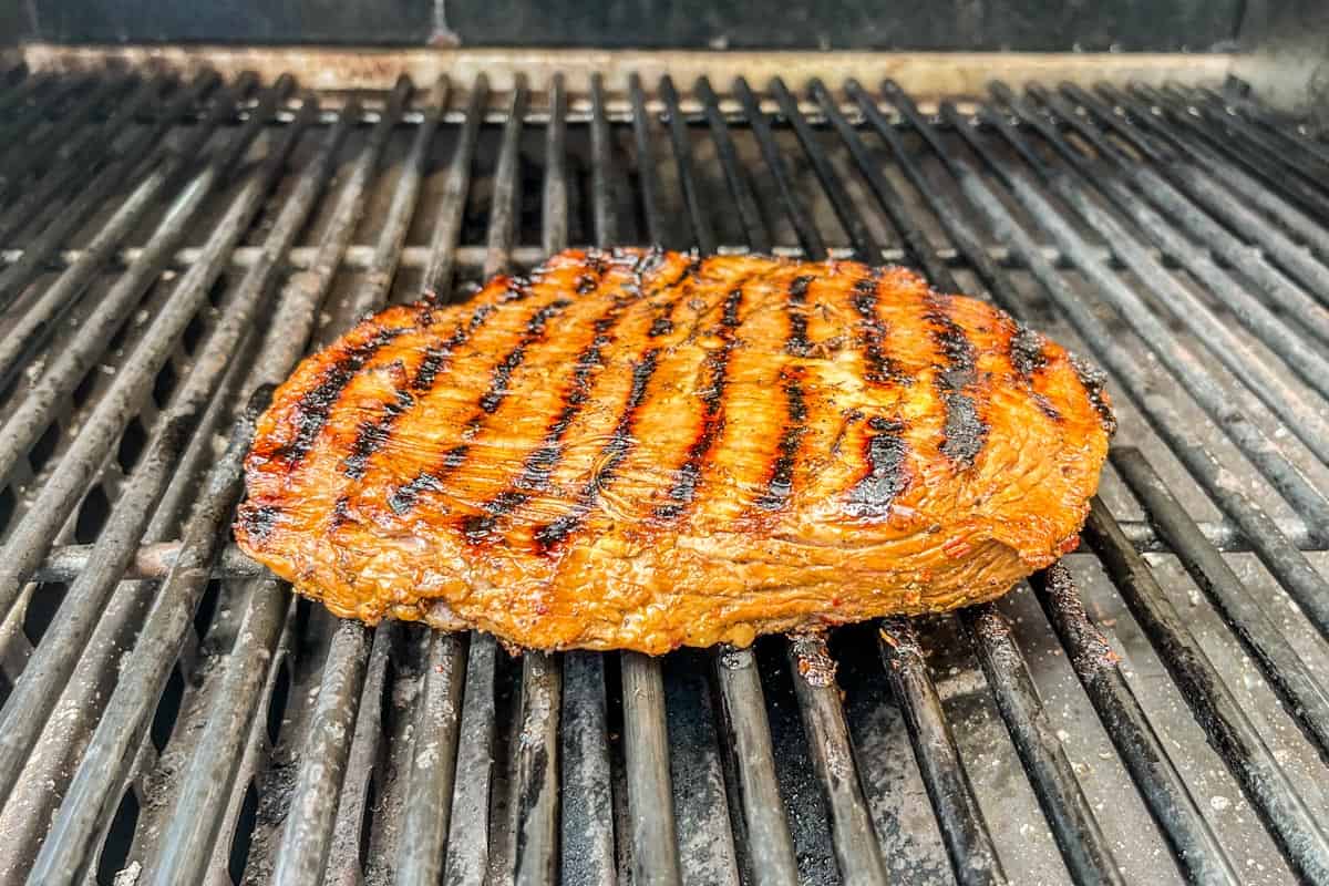 A marinated flank steak being grilled.