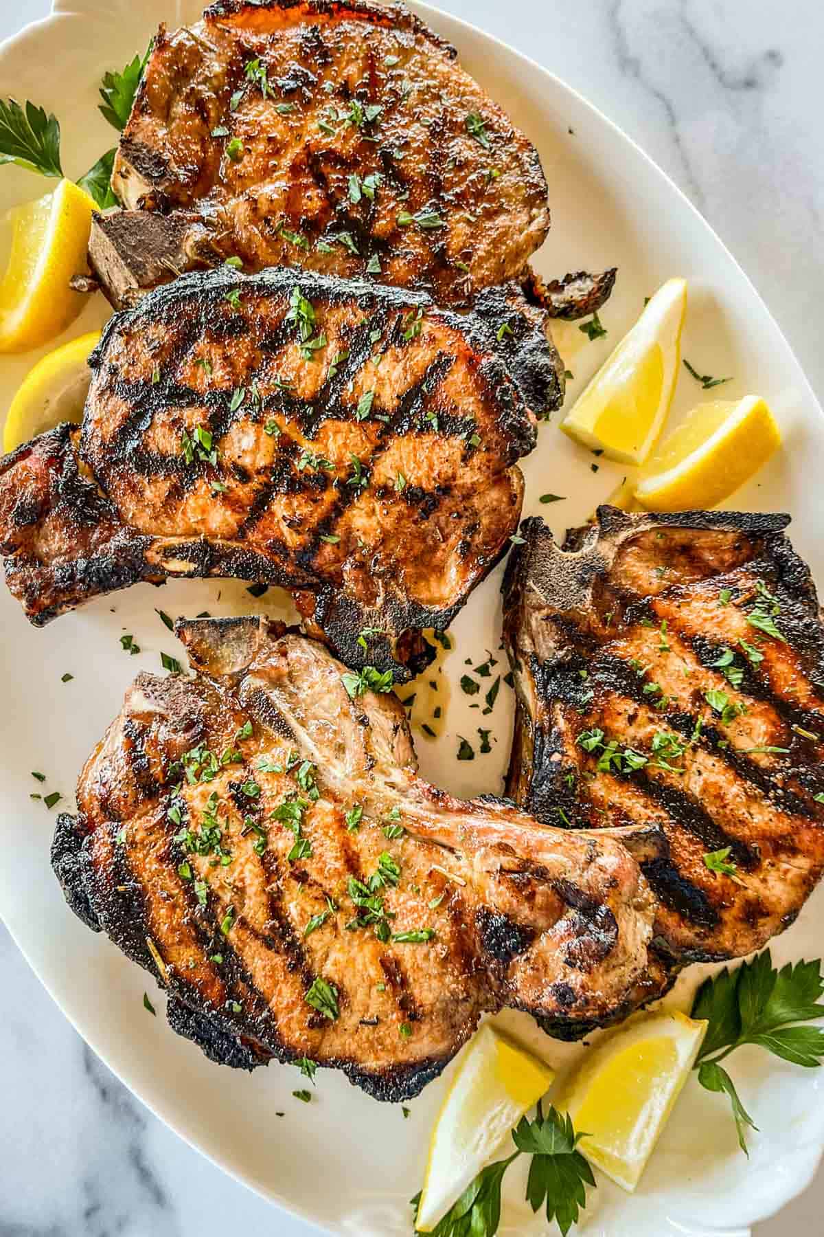 Grilled pork chops with lemons on a serving platter.