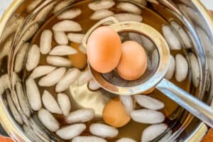 Eggs in a strainer being put in a bowl of ice water.