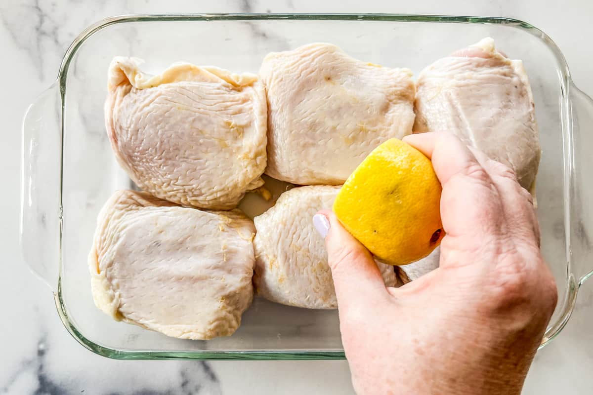 A lemon being squeezed on raw chicken thighs.