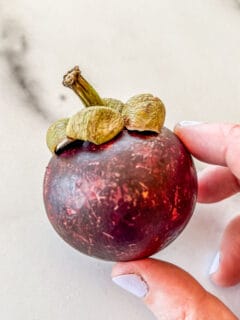 A mangosteen fruit being held in a hand.