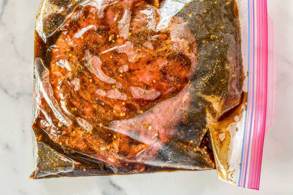 Flank steak with marinade in a plastic bag.