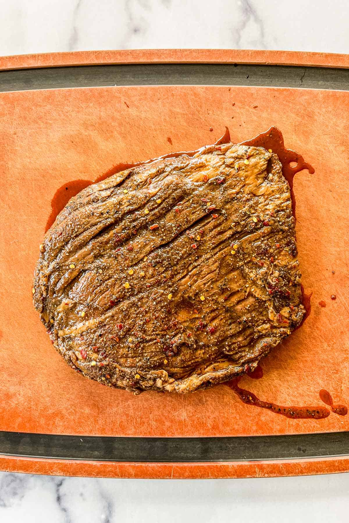 Marinated flank steak resting on a cutting board.