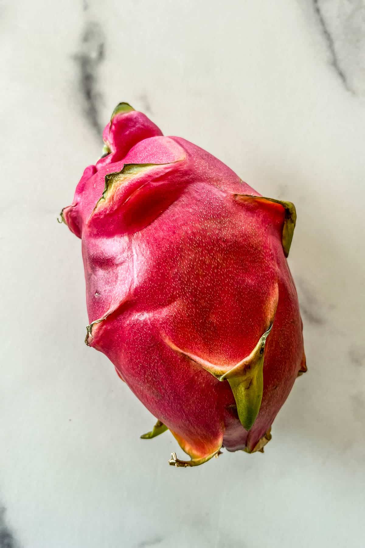 A pink dragon fruit on a marble background.
