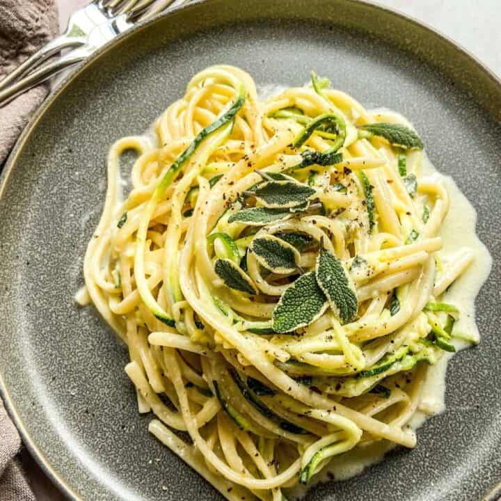 Creamy zucchini pasta on a dark plate.