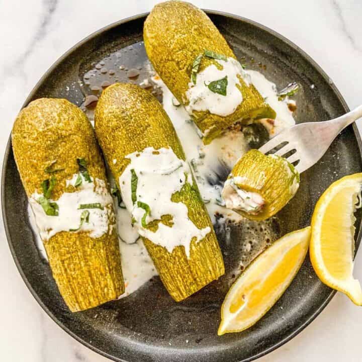 Kousa mahshi topped with yogurt on a black plate.