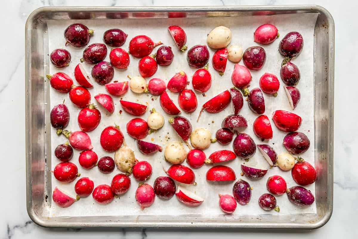 Radishes in a single layer on a parchment lined sheet pan.