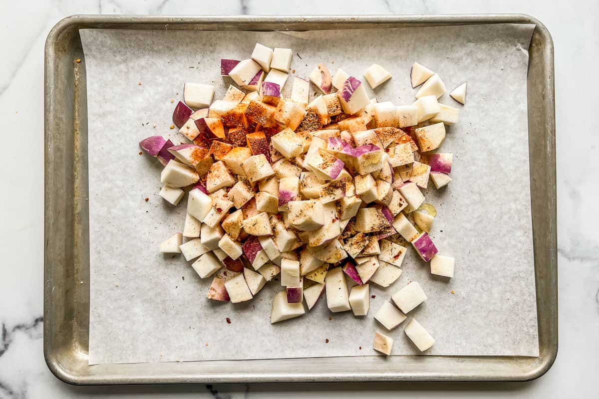 Chopped turnips topped with spices on a parchment lined baking sheet.