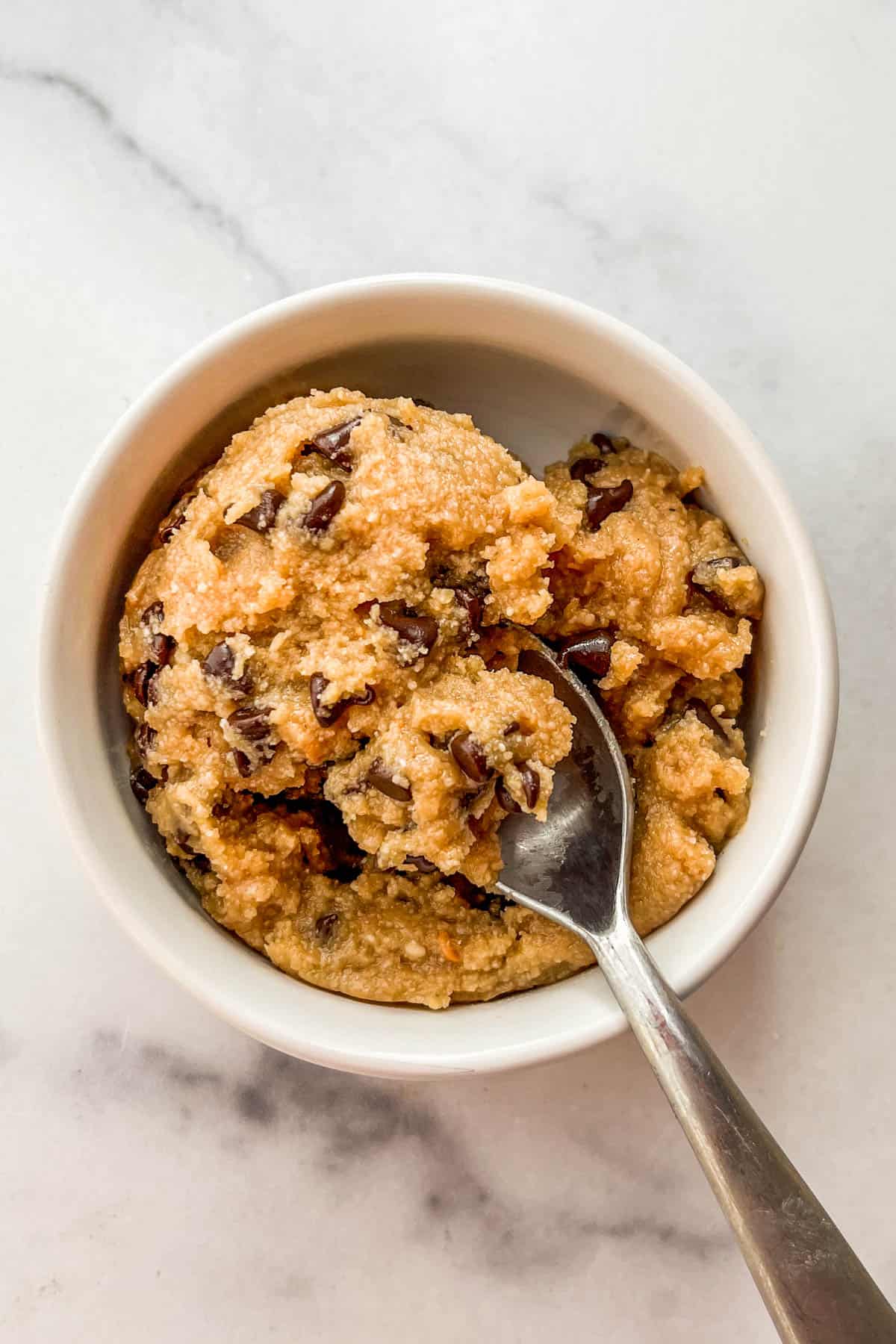 Healthy edible cookie dough with chocolate chips in a ramekin with a spoon.