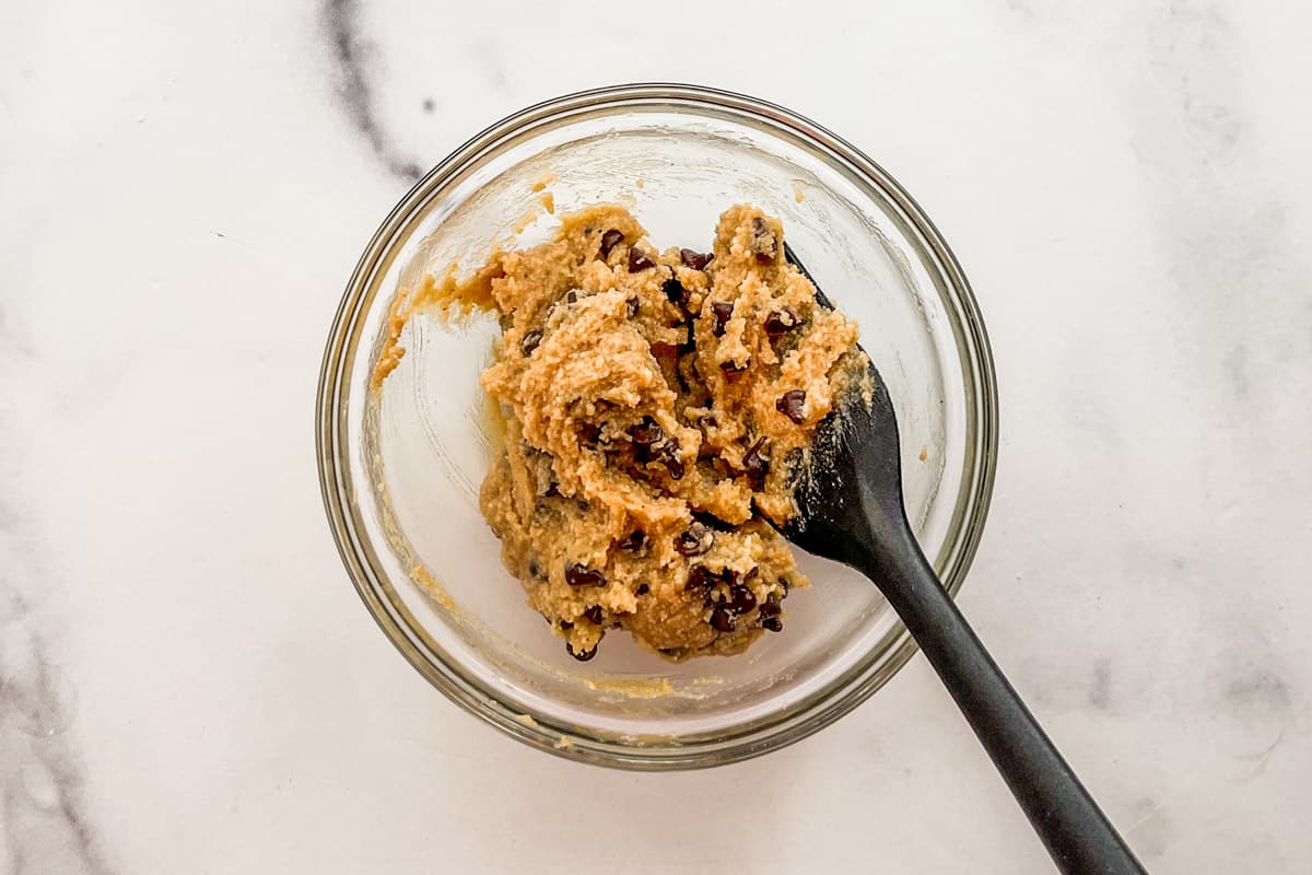 Chocolate chips being added to edible cookie dough.