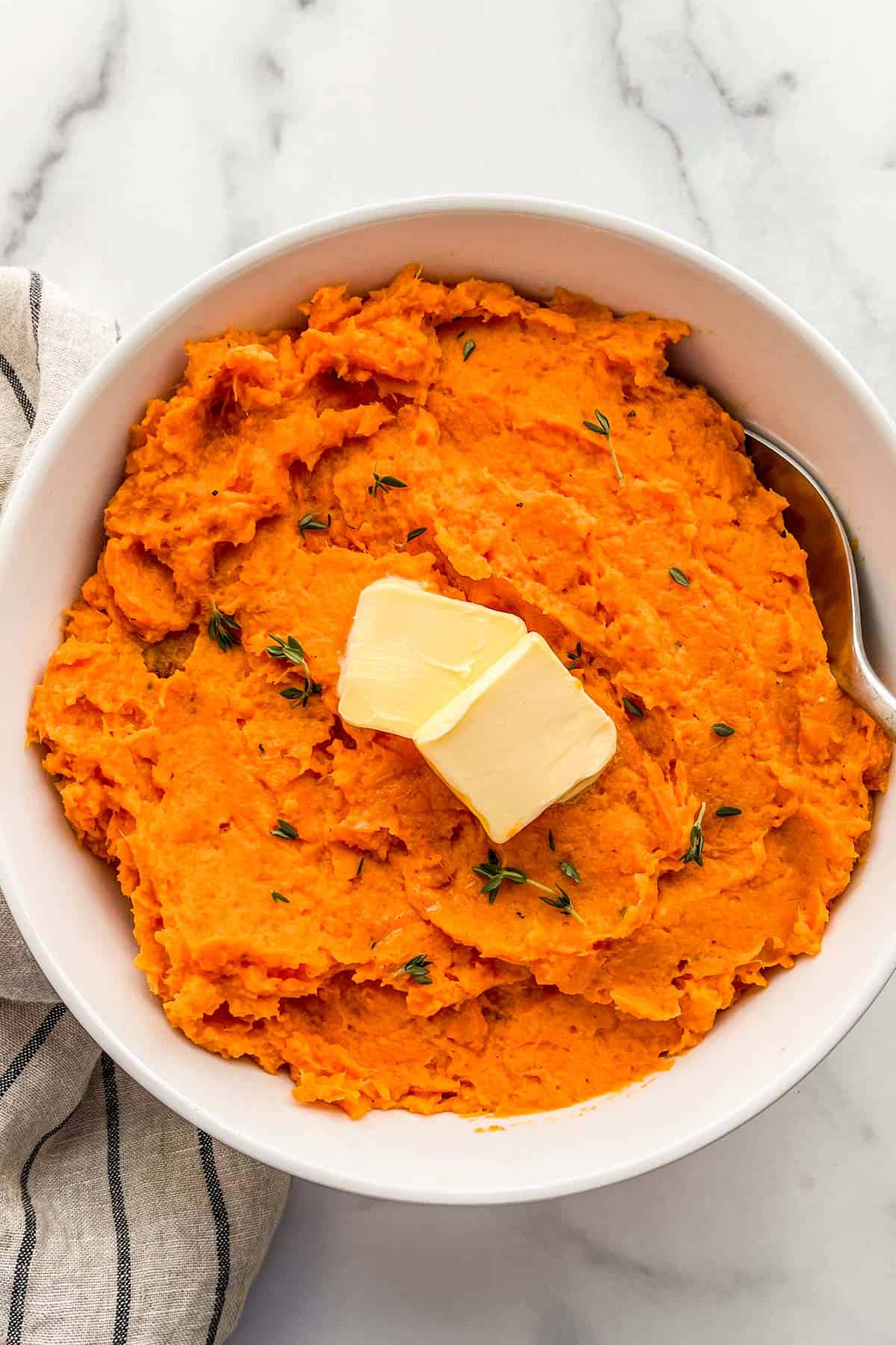 Healthy mashed sweet potatoes in a serving bowl topped with butter.