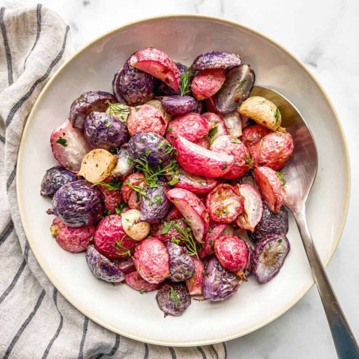 Roasted radishes in an off-white serving bowl with a spoon.