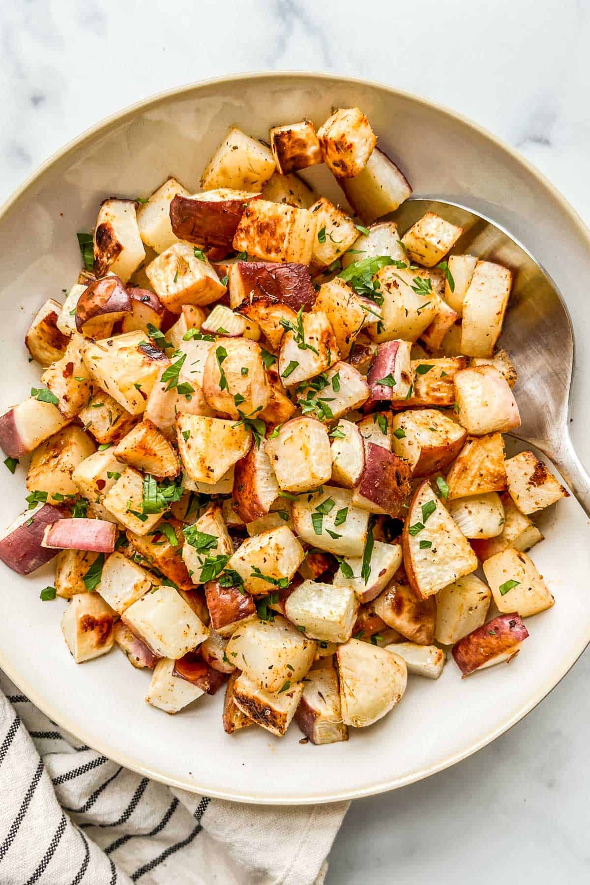 Oven roasted turnips in a serving bowl with a spoon.