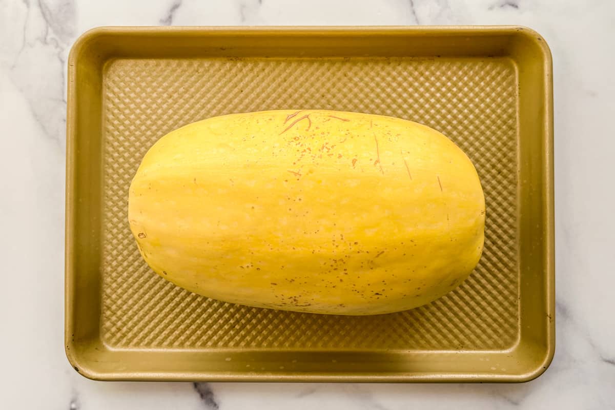 A whole spaghetti squash on a small baking sheet.