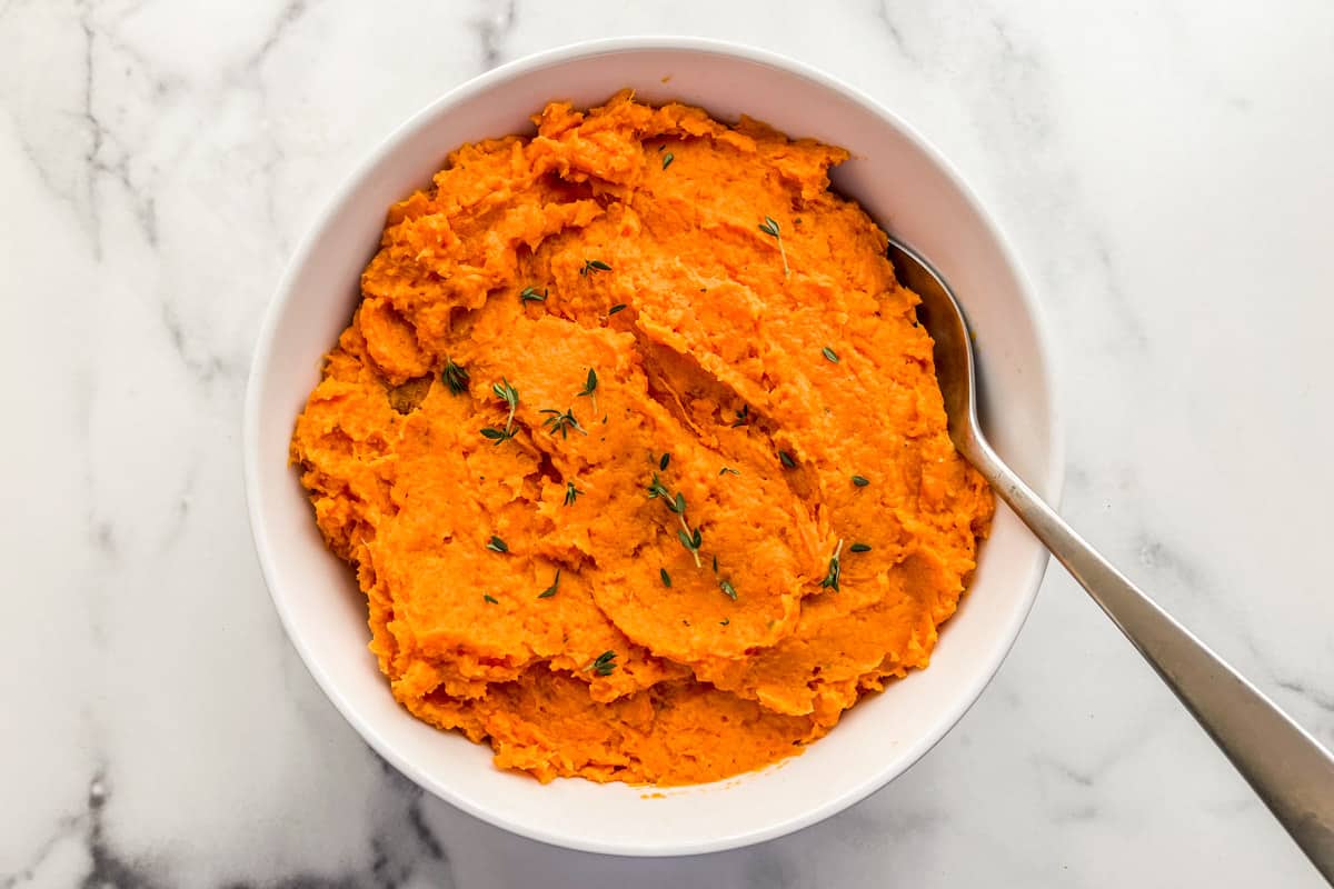 Mashed sweet potatoes in a serving bowl, topped with fresh thyme.