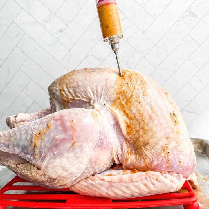 An injector of sauce being squeezed into a raw turkey.