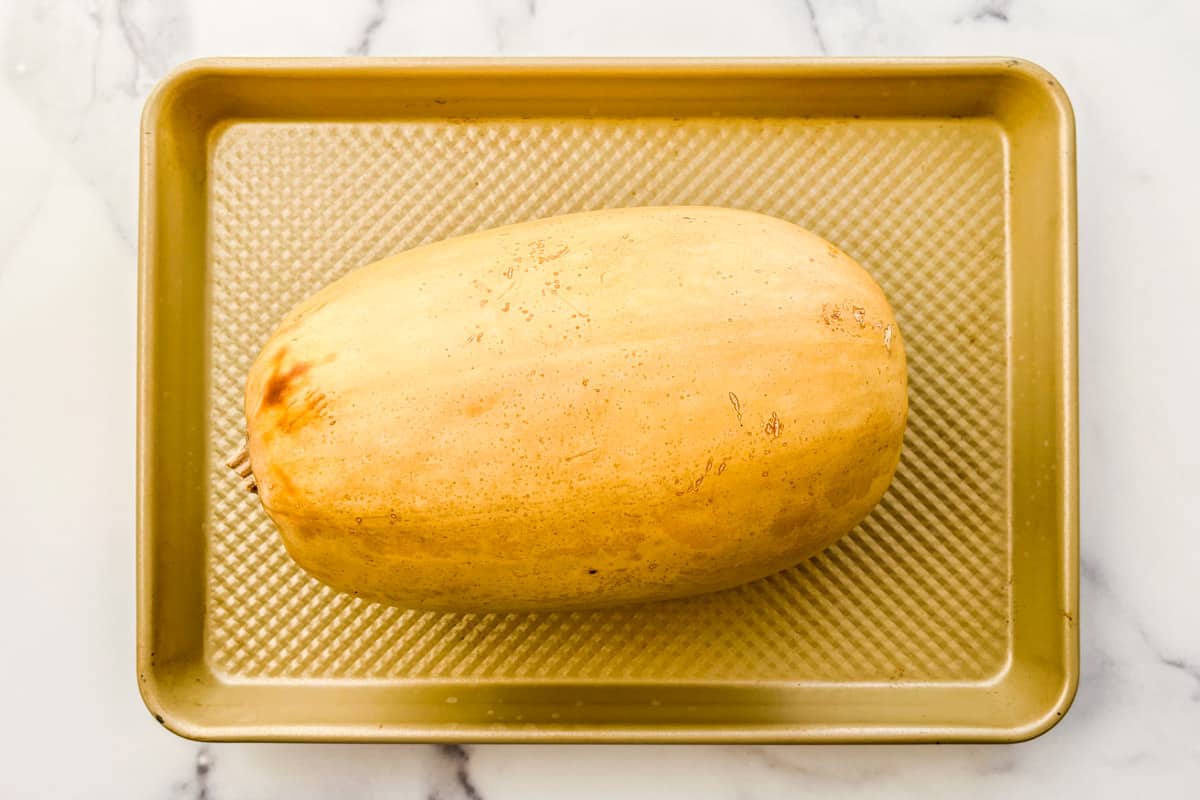 A whole roasted spaghetti squash on a baking sheet.