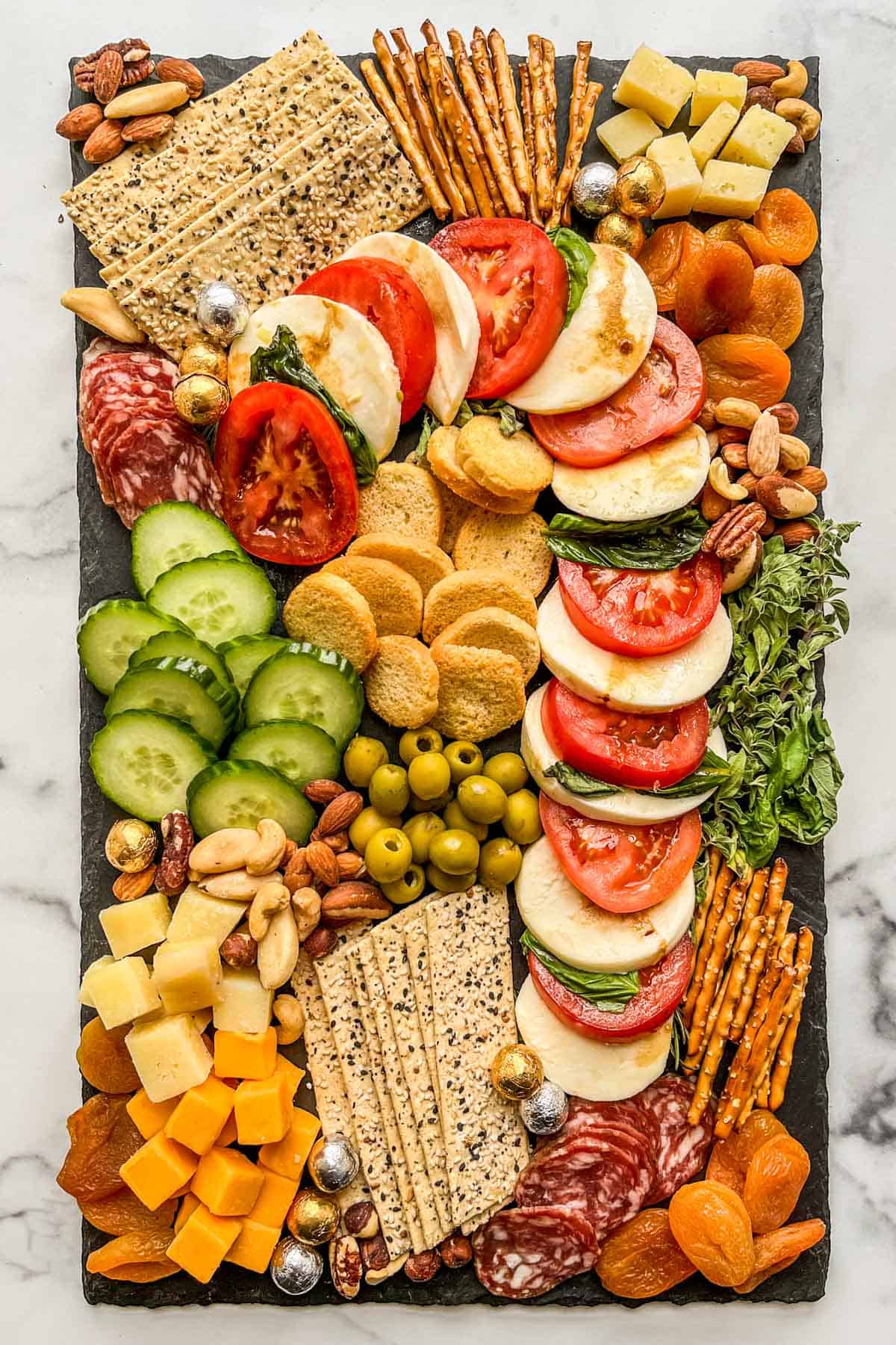 A Christmas appetizer platter with caprese, crackers, cheese, dried fruit, cucumbers, and pretzels.
