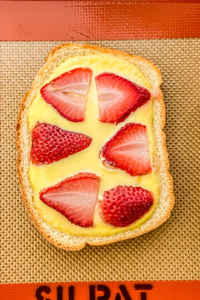 Custard toast topped with strawberries on a silpat baking sheet.